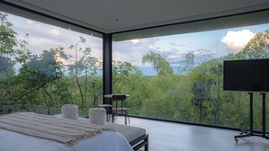 Une chambre moderne avec un grand lit, une télévision et une vue sur une forêt et des montagnes.