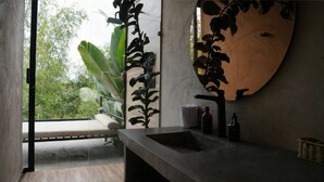 Une salle de bain moderne avec un grand miroir, un lavabo et une fenêtre donnant sur un espace verdoyant.