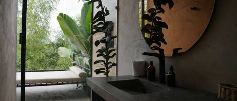 A modern bathroom with a large mirror, a sink, and a window overlooking greenery.