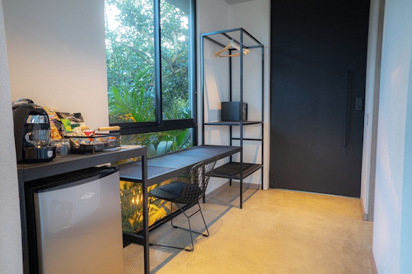 Una kitchenette compacta con refrigerador, cafetera y un pequeño comedor con una silla y mesa.