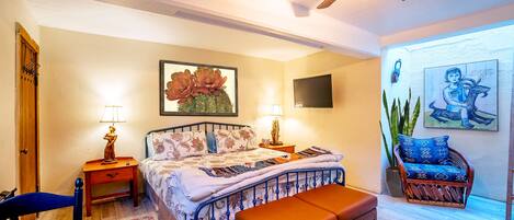 Quarto com cama, mesas de cabeceira, cadeira, banquinho, ventoinha no teto e obras de arte nas paredes.