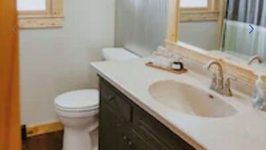 A small bathroom with a toilet, a sink, and a mirror. - Cozy Vacation Cottage on the Lake with Hot Tub!  (Webster)