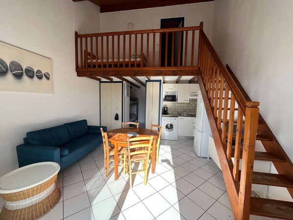 A compact living space with a dining area, a sofa, a washing machine, and a staircase.