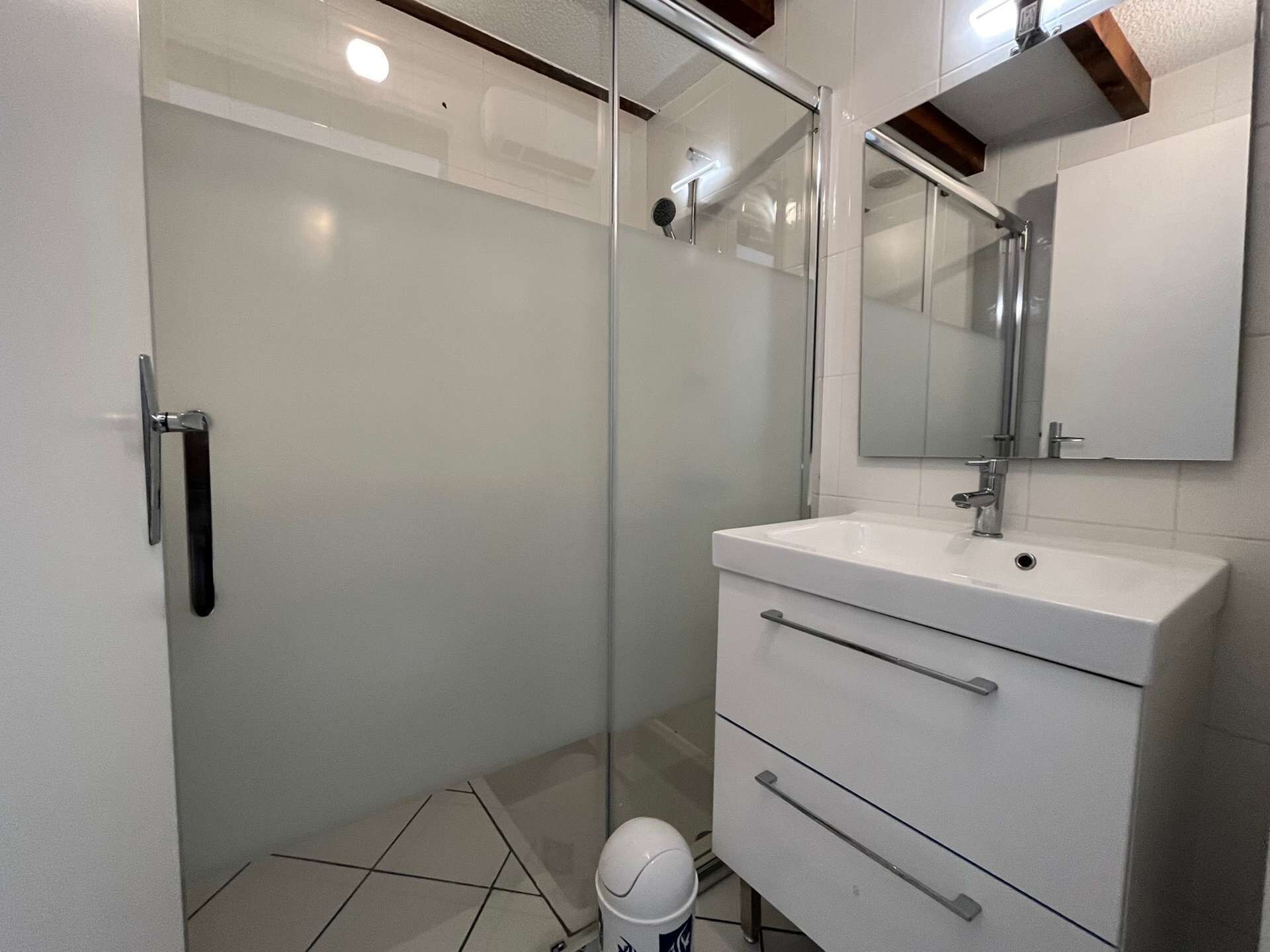 Une salle de bain moderne avec une douche à parois de verre, un lavabo blanc avec un miroir et un meuble blanc avec des tiroirs.