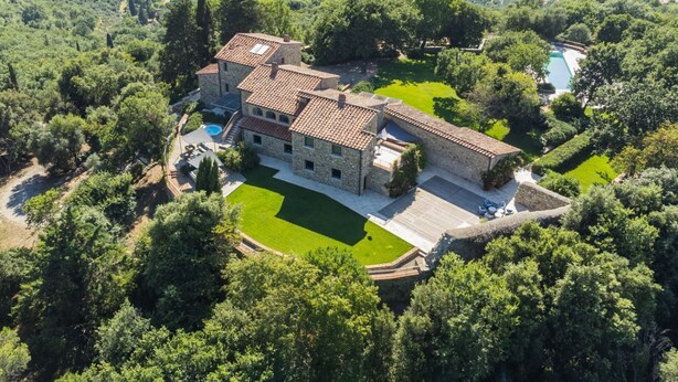 Une grande maison en pierre dotée d’une piscine, entourée d’une végétation luxuriante et de vignobles.
