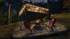 Een houten terras met Adirondack-stoelen en een vuurkuil, omringd door een stenen rand.