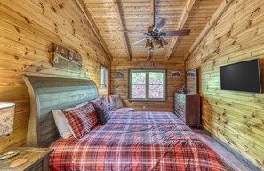 Een slaapkamer in een houten chalet met een bed, een plafondventilator, een dressoir en een televisie.