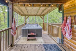 Een houten terras met een jacuzzi, houten leuningen en uitzicht op het bos.