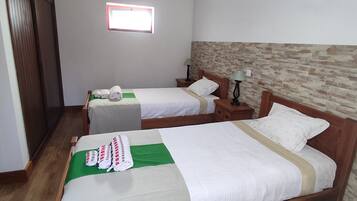 A hotel room with two beds, wooden headboards, a small window, and a stone-patterned wall.