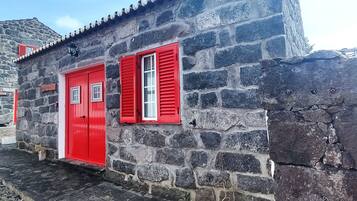 A stone building with red doors and shutters, featuring a small window and a sign on the wall.