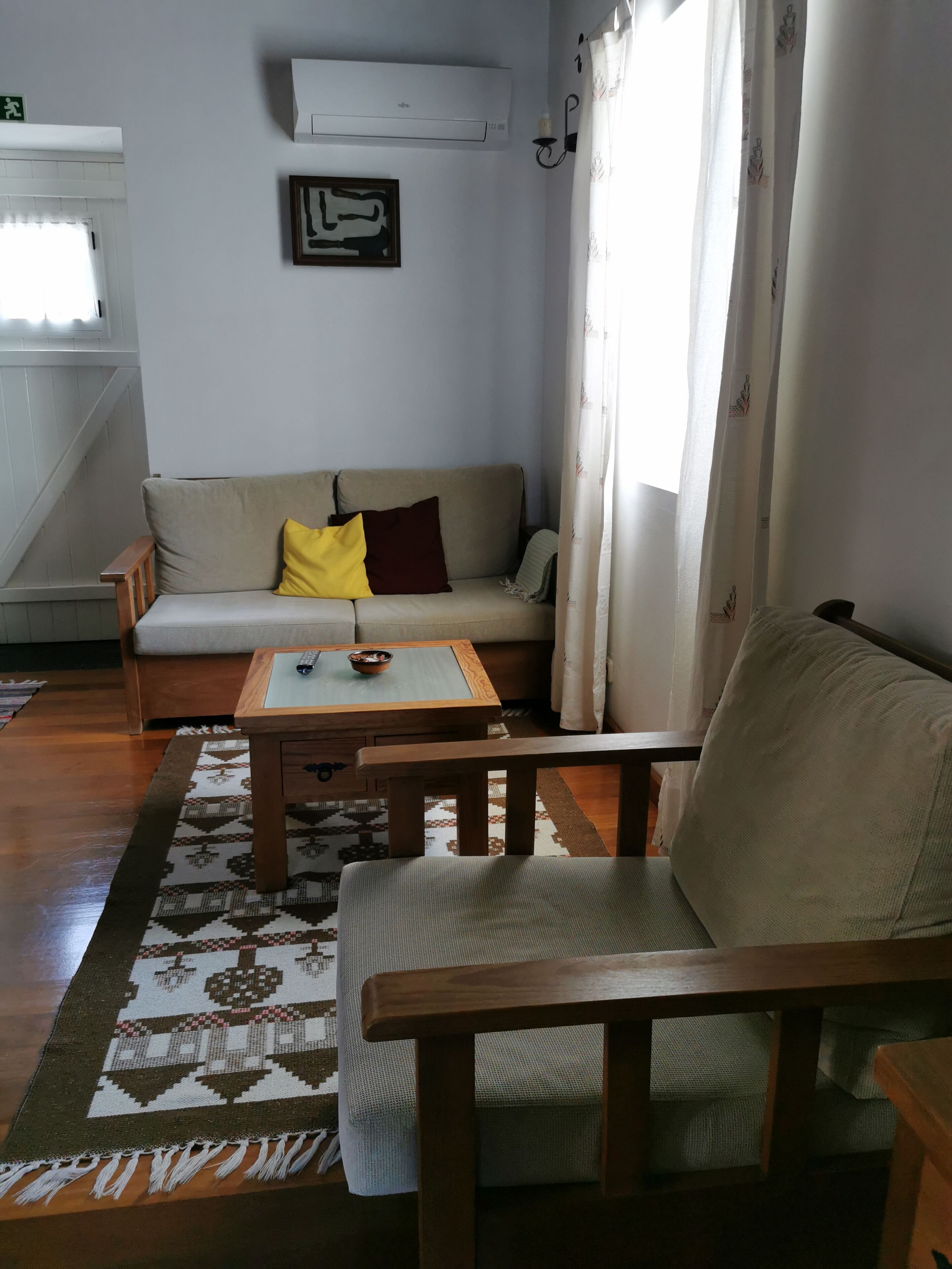 Una sala de estar con un sofá, una silla de madera, una mesa de centro y un tapete estampado.