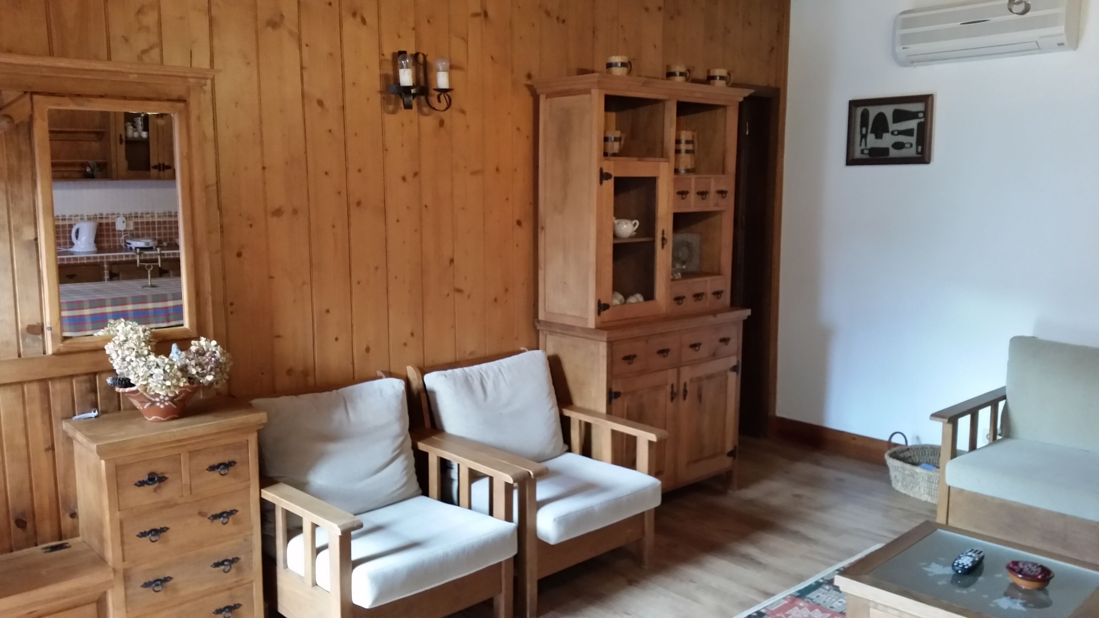 A wooden-paneled room with a sofa, a cabinet with drawers, a small table with a remote control, and a wall-mounted air conditioner.