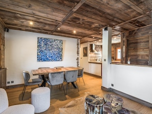 A dining area with a wooden table and chairs, a large abstract painting, and a kitchen in the background. - Appartement Amédé - Welkeys (Megève)