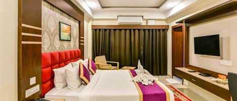 Quarto de hotel com uma cama, uma mesa com telefone, uma televisão e um ventilador de teto.