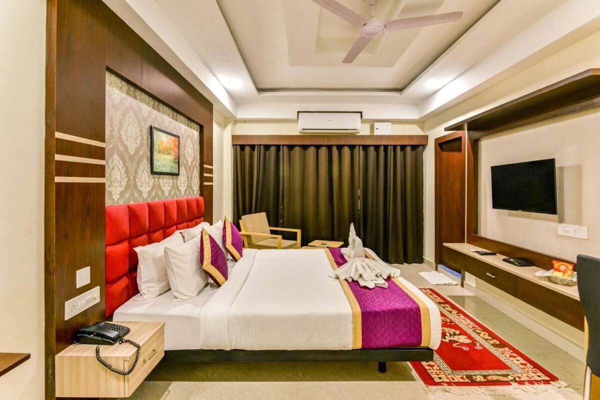 Una habitación de hotel con una cama, un escritorio con teléfono, un televisor y un ventilador de techo.