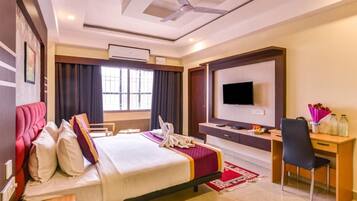 Habitación de hotel con cama, escritorio, televisión y ventilador de techo.