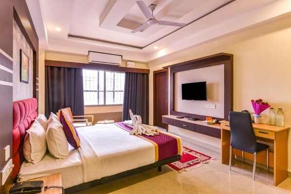 A hotel room with a bed, desk, TV, and ceiling fan. - Mount Amara Hotel & Spa (Jalpaiguri)