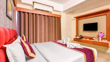 A hotel room with a bed, curtains, a flat-screen TV, a wooden dresser, and a wall-mounted air conditioner.