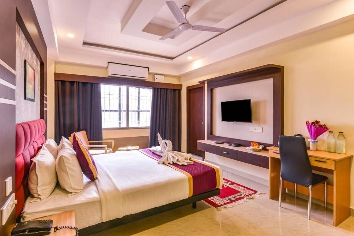 Habitación de hotel con cama, escritorio, televisión y ventilador de techo.