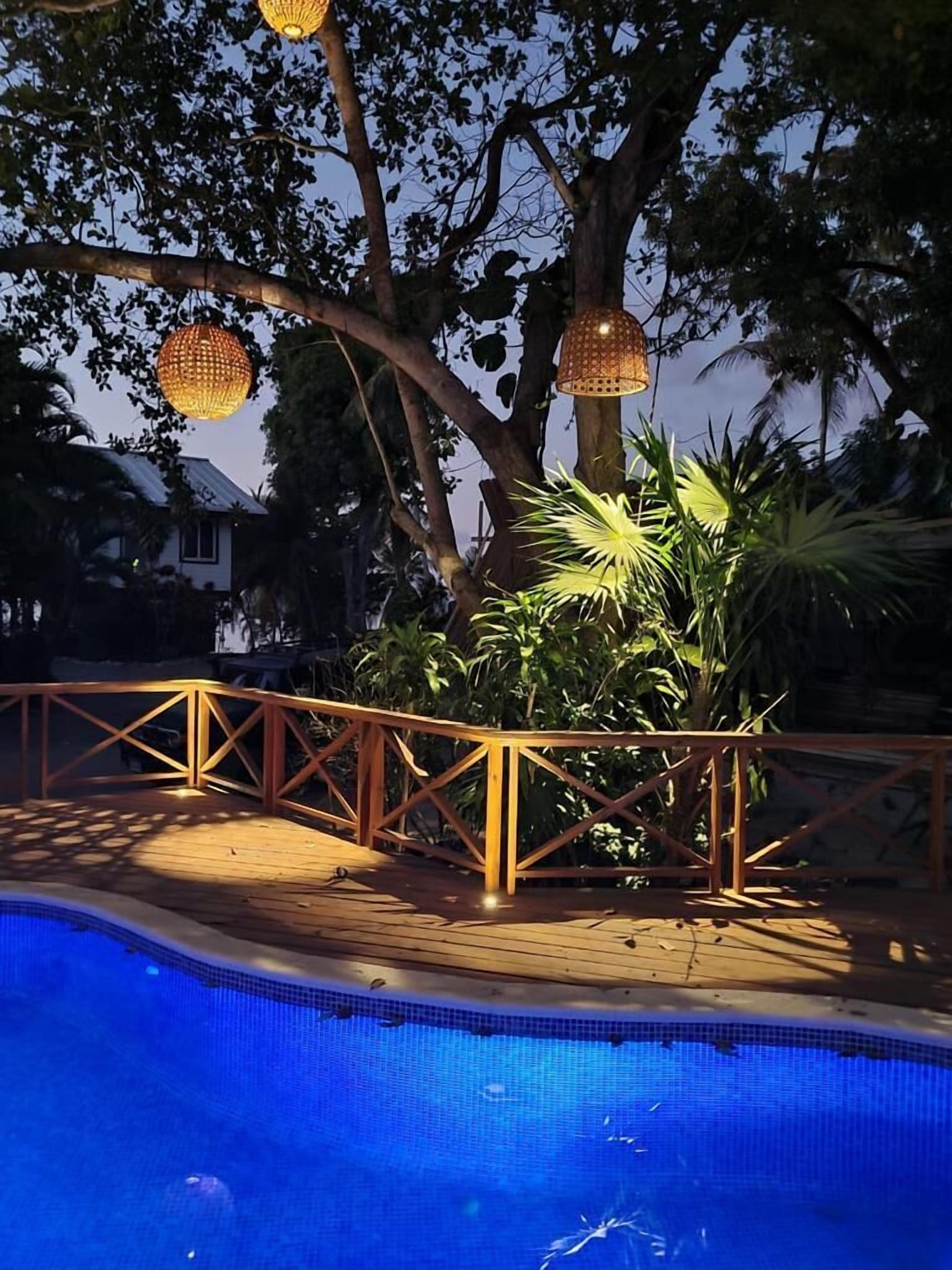 Uma área de piscina com um deque de madeira, guarda-corpo de metal e lanternas penduradas.