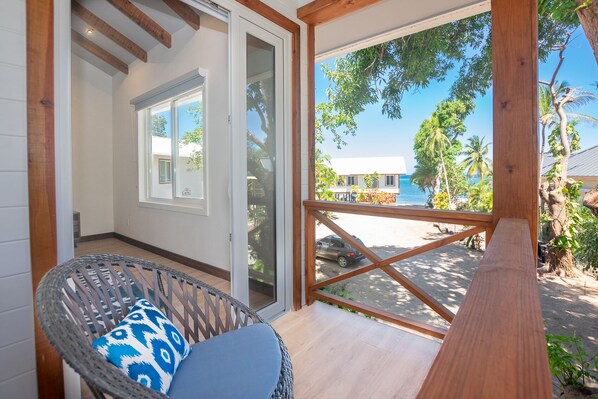 A room with a wicker chair, a wooden bench, and a view of a beach and palm trees.