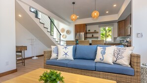 Un salon moderne avec un canapé bleu, des meubles en osier et un escalier menant à l’étage supérieur.