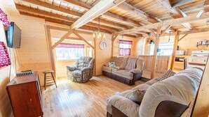 A wooden cabin interior with a wooden floor, a sofa, a chair, a small table, and a television.