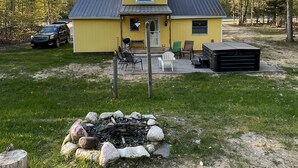 A yellow building with a metal roof, surrounded by trees and a fire pit.