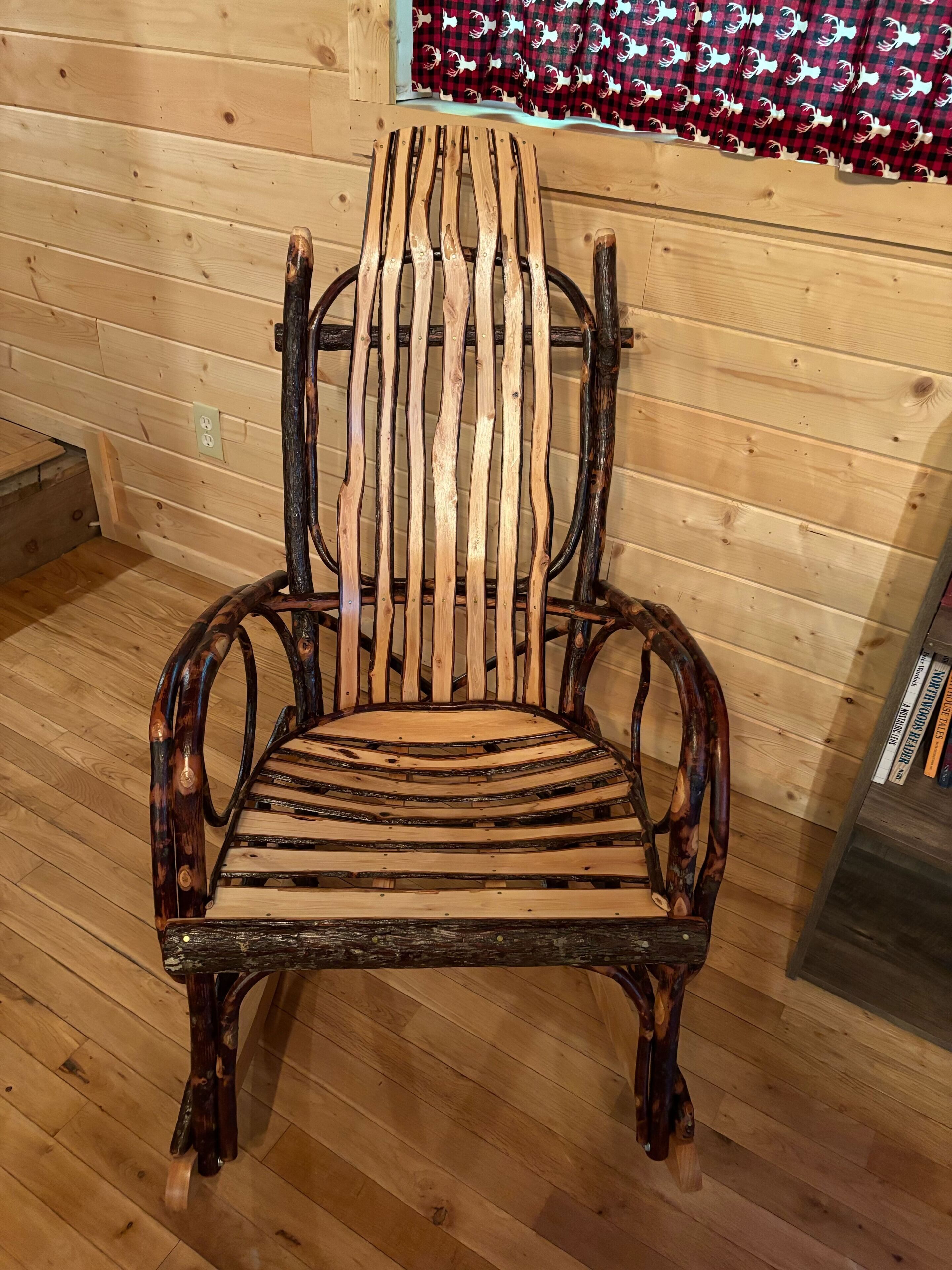 A rustic wooden chair with a unique slatted backrest and curved armrests, placed in a room with wooden flooring and walls.
