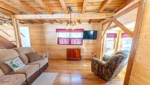 A cozy wooden cabin interior with a sofa, armchair, and a TV mounted on the wall.