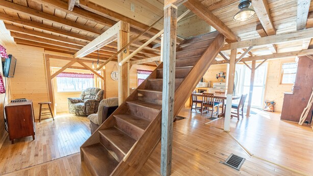 A spacious wooden interior with a central staircase, wooden floors, and a dining area with chairs and tables.