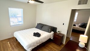 Ein Schlafzimmer mit einem Bett, einem Nachttisch, einem Deckenventilator, einem Fenster und einer Tür zu einem anderen Raum.