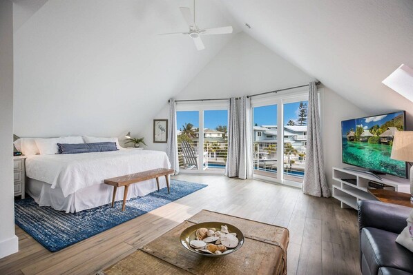 Ein Schlafzimmer mit einem großen Bett, einem Fernseher und einem Balkon mit Blick auf einen Pool.