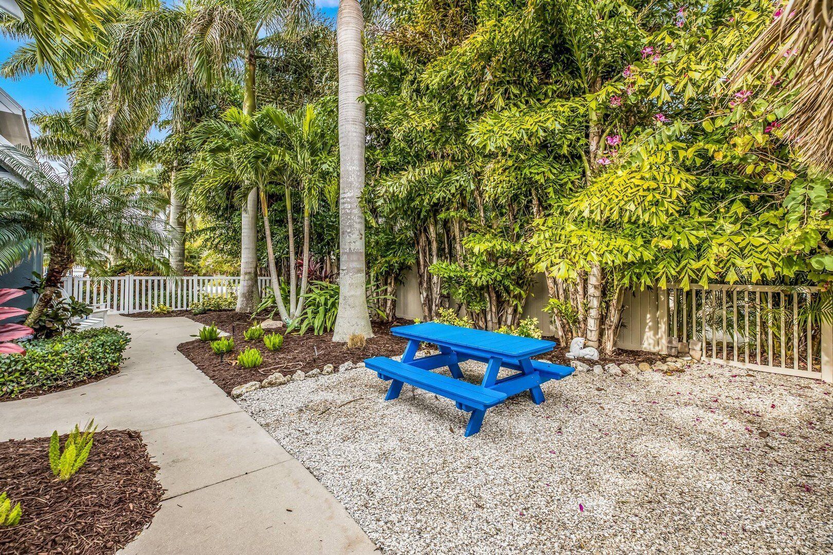A garden with a blue picnic table, surrounded by various plants and trees.