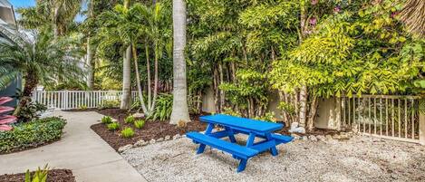 A garden with a blue picnic table, surrounded by various plants and trees.