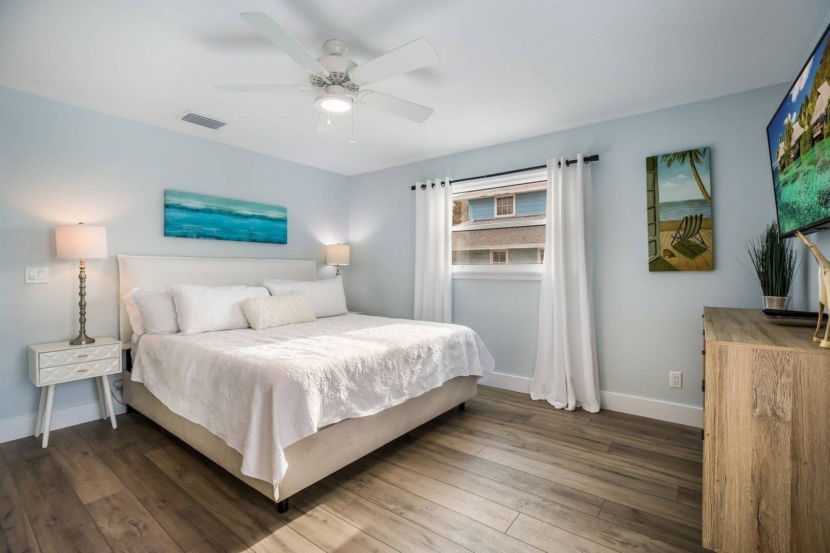 A bedroom with a bed, nightstands, a ceiling fan, a window with curtains, and a painting on the wall.