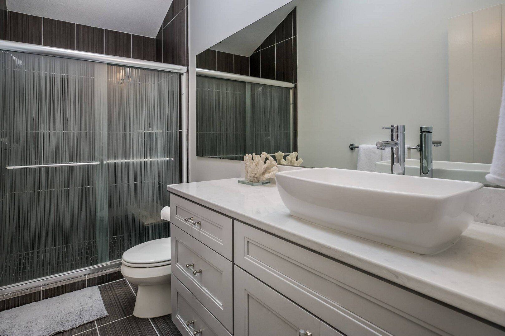Une salle de bain moderne avec un grand lavabo blanc, des toilettes et une douche à l’italienne dotée de parois de verre verticales.