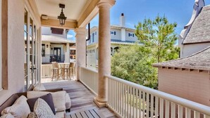 A covered porch with a seating area, a dining table, and a view of neighboring houses. - Lady Martinique | Exquisite 5 Bedroom with Private Pool, Outdoor Fireplace (Rosemary Beach)