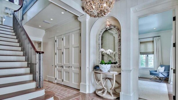 A grand staircase leading to a landing with a decorative mirror and a round table with a vase of flowers. - Lady Martinique | Exquisite 5 Bedroom with Private Pool, Outdoor Fireplace (Rosemary Beach)