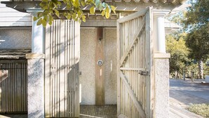 A wooden gate with a metal latch, leading to a covered outdoor area with a pergola overhead. - Cozy cottage nestled in forest on BHI. Close to east beach and located in tranquil Sumners Crescent (Bald Head Island)