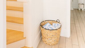 A staircase with wooden steps leading to a white-walled room. A woven basket with folded towels is placed on the floor near the stairs. - Cozy cottage nestled in forest on BHI. Close to east beach and located in tranquil Sumners Crescent (Bald Head Island)