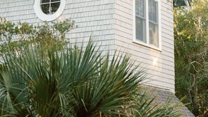 A house with a gabled roof, a circular window, and a rectangular window. - Cozy cottage nestled in forest on BHI. Close to east beach and located in tranquil Sumners Crescent (Bald Head Island)
