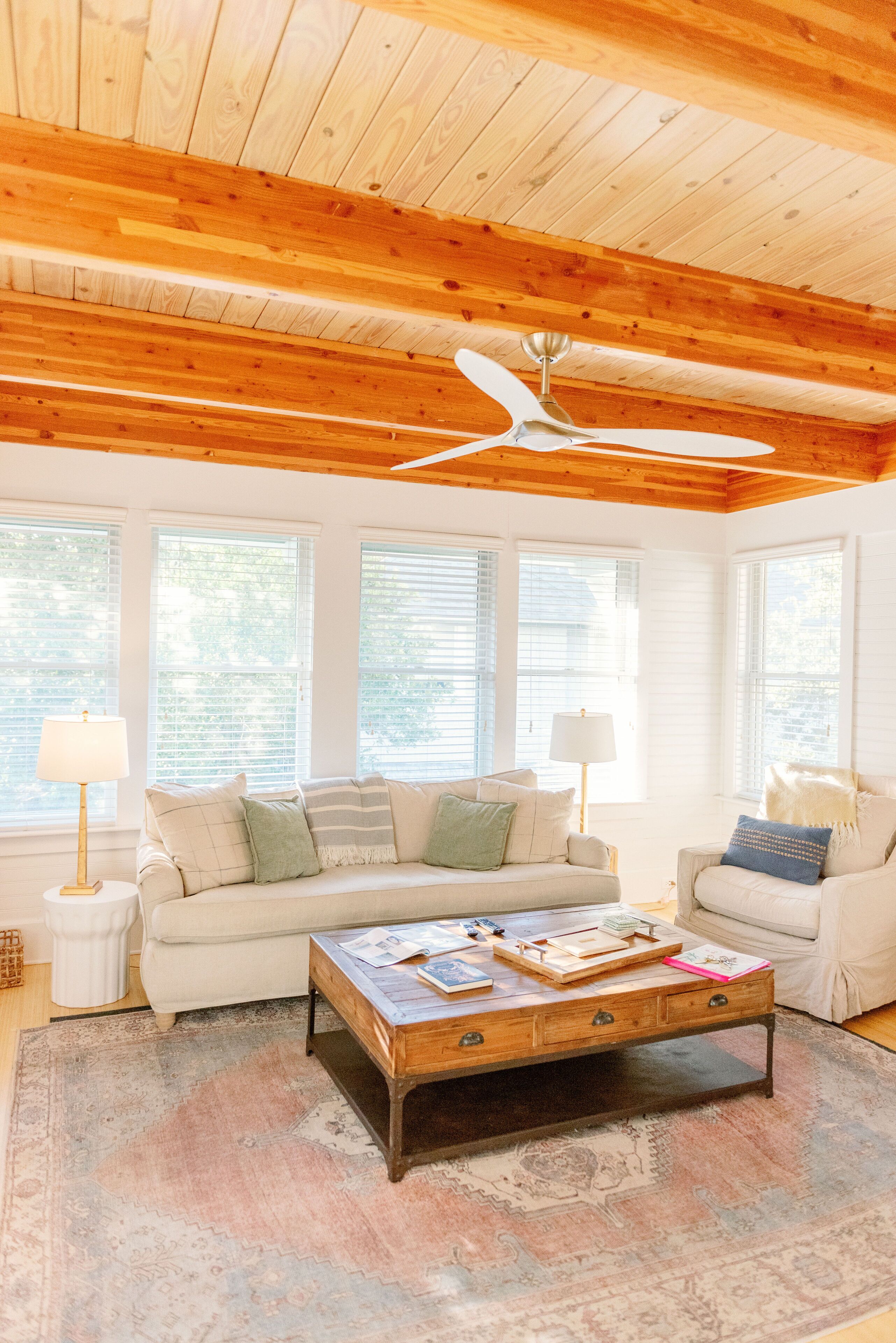 A cozy living room with a wooden ceiling, a ceiling fan, a sofa, a coffee table, and a patterned rug.