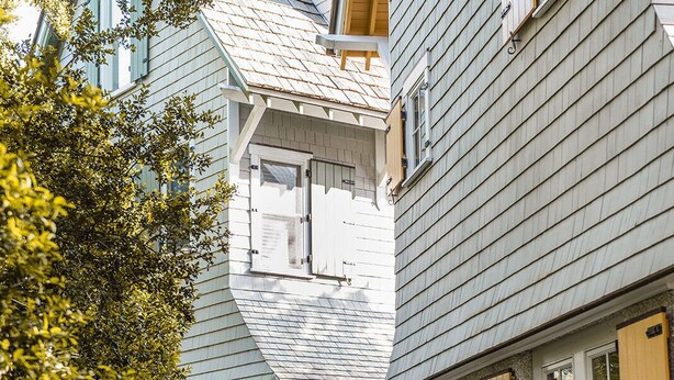 A residential building with a covered walkway, a stone wall, and a wooden door. - Cozy cottage nestled in forest on BHI. Close to east beach and located in tranquil Sumners Crescent (Bald Head Island)