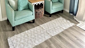 Una sala de estar con dos sillones azul verdosos, una mesita de noche con una planta, un televisor de pantalla plana en la pared y un ventanal con cortinas.