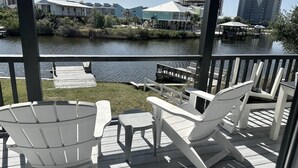 Una terraza con sillas Adirondack blancas y una pequeña mesa, con vistas a un cuerpo de agua con muelles y edificios al fondo.