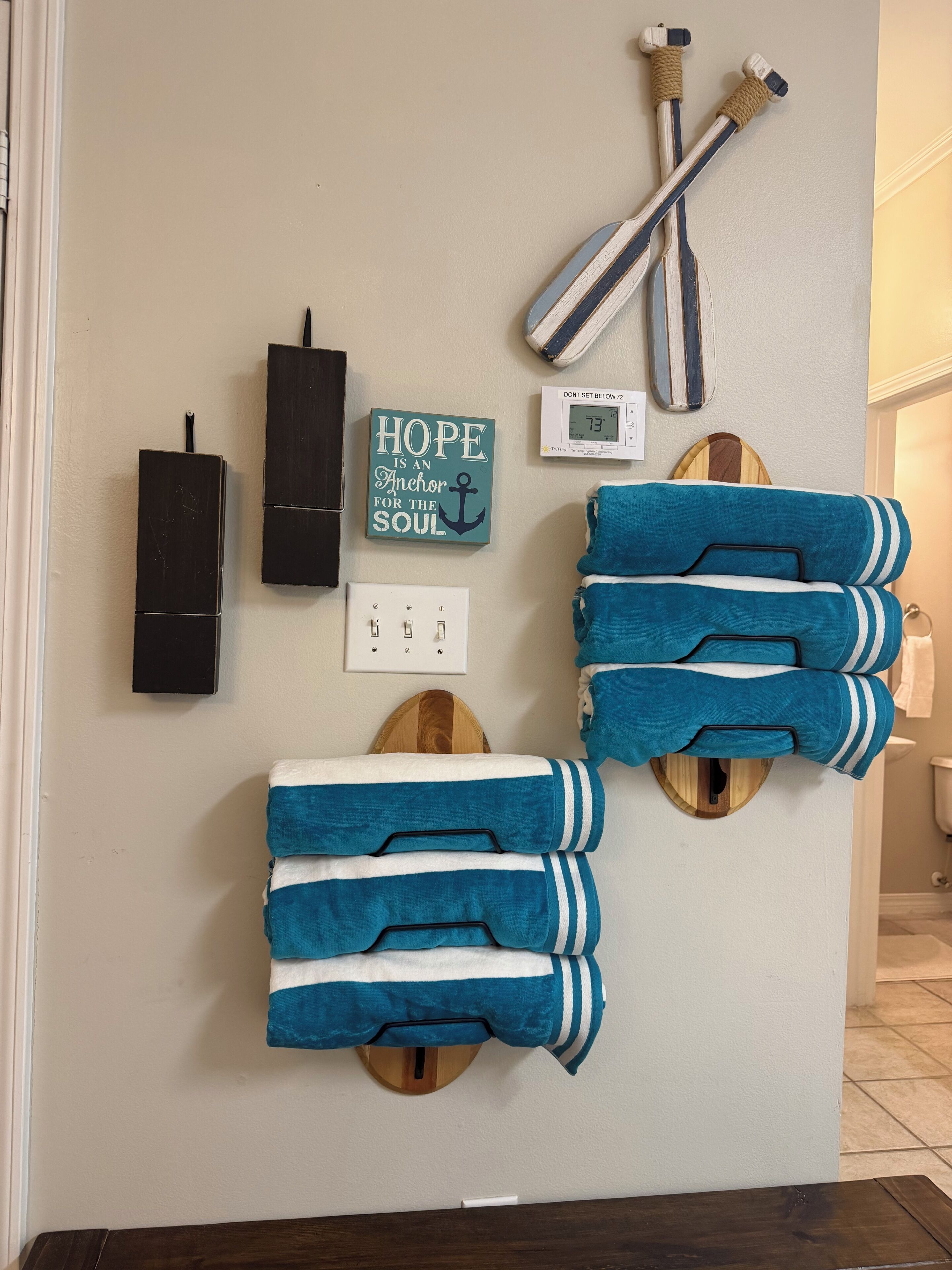 A bathroom with towels, a wall clock, a thermostat, and a motivational quote.