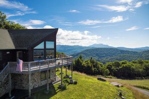 A stone building with a balcony, an American flag, and a view of mountains. - Mountaintop Cabin with Majestic Views - Hot Tub + Game Room + Pet Friendly (Newland)