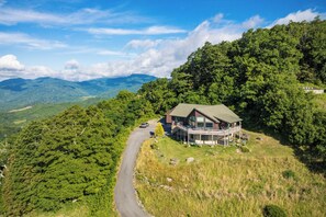 Eine Lodge mit einer großen Veranda und zahlreichen Fenstern, umgeben von üppiger Vegetation und Bergen im Hintergrund.