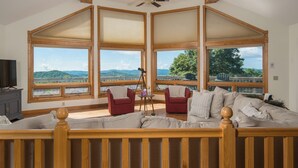 Une pièce spacieuse avec un grand lit, deux fauteuils rouges, un ventilateur de plafond en bois et de grandes fenêtres donnant sur l’extérieur.